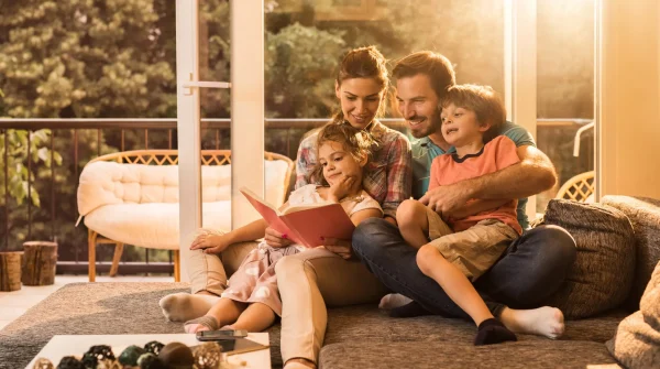 Glückliche Familie sitzt gemeinsam auf dem Sofa und liest – Symbolbild für Sicherheit durch sinnvolle Versicherungen