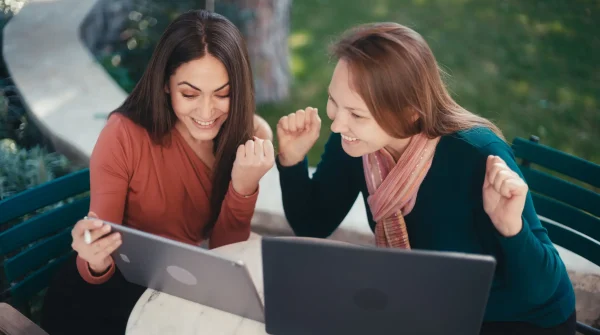 Zwei Frauen freuen sich gemeinsam vor ihren Laptops über eine erfolgreiche Entscheidung – Symbolbild für finanzielle Unabhängigkeit durch Fondsrente.