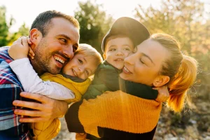 Glückliche Familie mit zwei kleinen Kindern umarmt sich lachend im Sonnenlicht im Freien