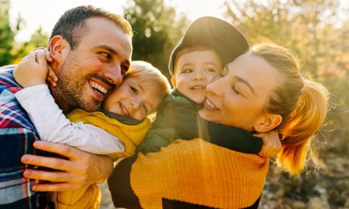 Glückliche Familie mit zwei kleinen Kindern umarmt sich lachend im Sonnenlicht im Freien