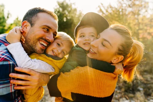 Glückliche Familie mit zwei kleinen Kindern umarmt sich lachend im Sonnenlicht im Freien