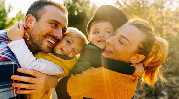 Glückliche Familie mit zwei kleinen Kindern umarmt sich lachend im Sonnenlicht im Freien