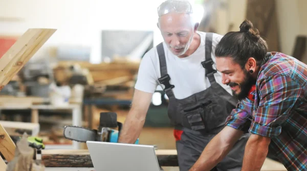 Zwei Handwerker in einer Werkstatt betrachten gemeinsam einen Laptop – Symbolbild für die Gewerbeversicherung