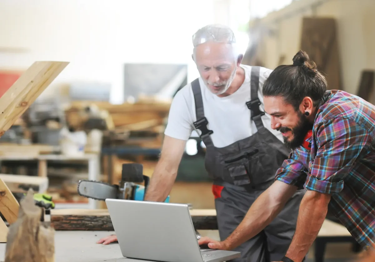 Zwei Handwerker in einer Werkstatt betrachten gemeinsam einen Laptop – Symbolbild für die Gewerbeversicherung