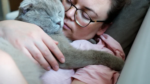 Eine Frau hält ihre kranke Katze liebevoll im Arm – beide liegen auf dem Sofa, eng aneinandergeschmiegt und in einem ruhigen Moment vereint.