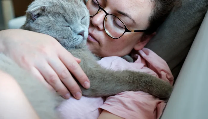 Eine Frau hält ihre kranke Katze liebevoll im Arm – beide liegen auf dem Sofa, eng aneinandergeschmiegt und in einem ruhigen Moment vereint.