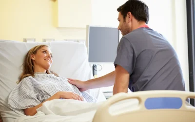 Lächelnde Patientin liegt im Krankenhausbett und spricht mit einem Arzt in moderner Klinikumgebung