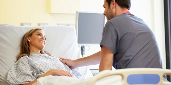 Lächelnde Patientin liegt im Krankenhausbett und spricht mit einem Arzt in moderner Klinikumgebung