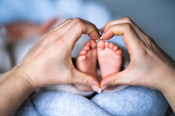 Zwei erwachsene Hände formen ein Herz um die Füße eines Neugeborenen – Symbolbild für Kinderwunsch und künstliche Befruchtung