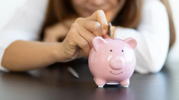 Frau wirft Geldstück in ein rosa Sparschwein – Symbolbild für private Rentenversicherung und persönliche Vorsorge