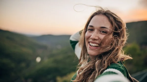Junge Frau macht ein Selfie in der Natur bei Sonnenuntergang und genießt sorglos den Moment dank frühzeitiger Vorsorge