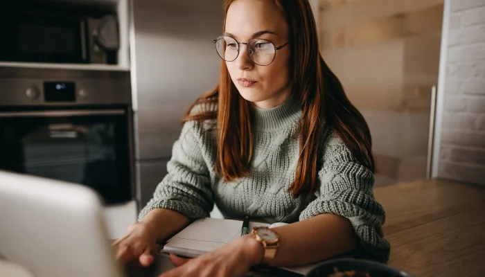 Frau sitzt nachdenklich vor dem Laptop, prüft Unterlagen – Symbol für Recherche zur Berufsunfähigkeitsversicherung und Leistungsbeginn.